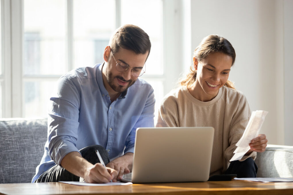 Happy couple using laptop, calculating domestic bills, mortgage or loan documents, smiling woman holding papers, family planning budget, managing household expenses, focused man filling form