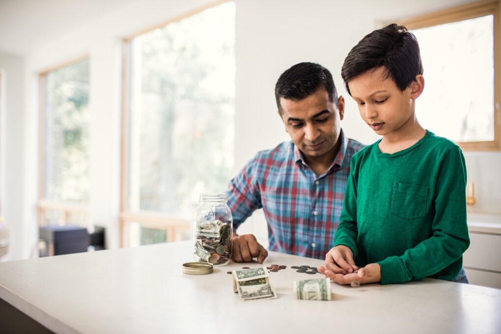 Father and young son sitting at kitchen counter counting money